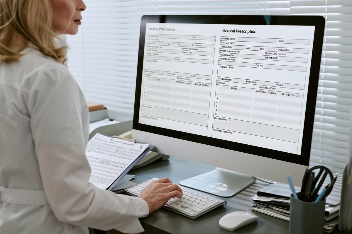 Doctor reviewing digital prescription forms on desktop computer, managing patient records